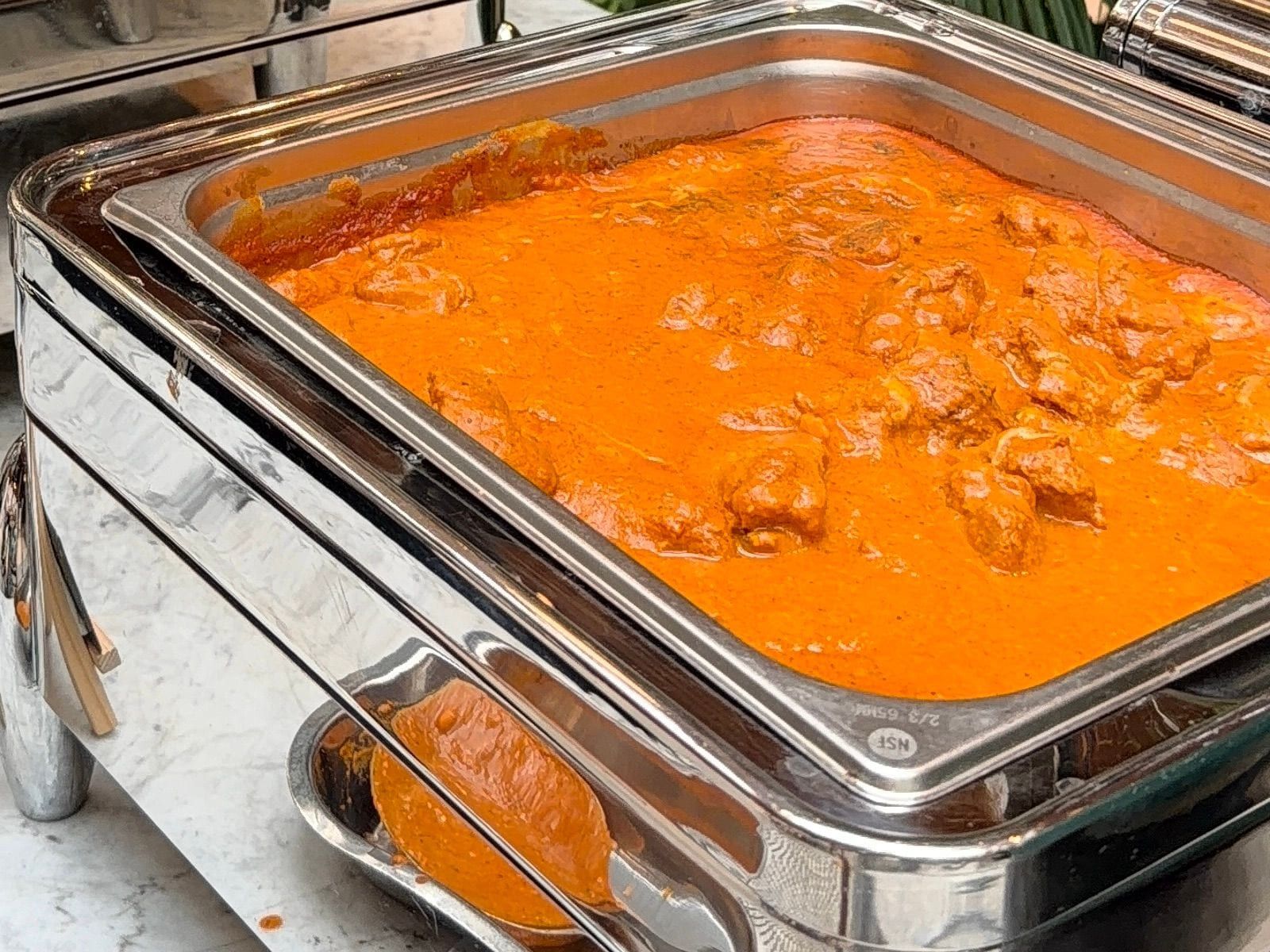 Butter chicken kept warm in a steel chafing dish at a buffet