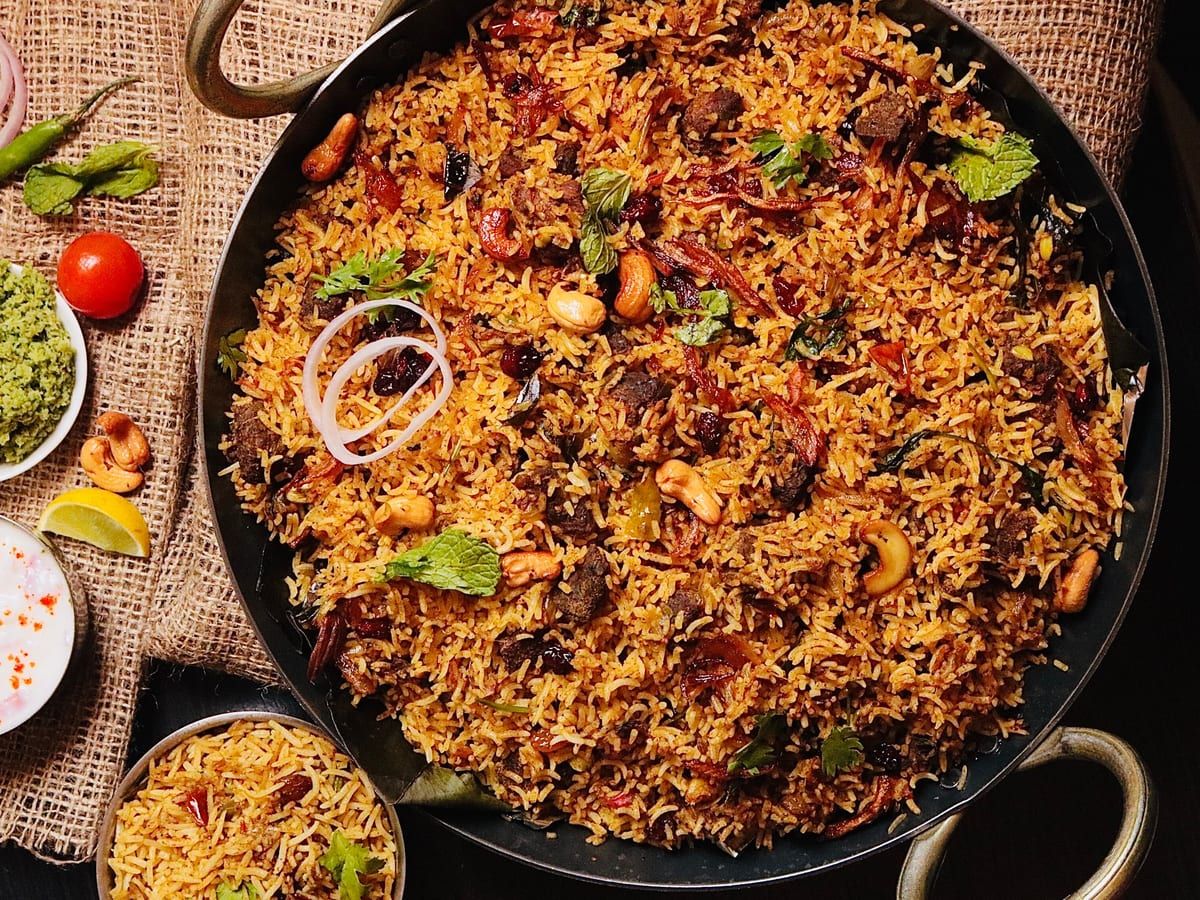 Dum biryani with cashews and herbs in a wide pan