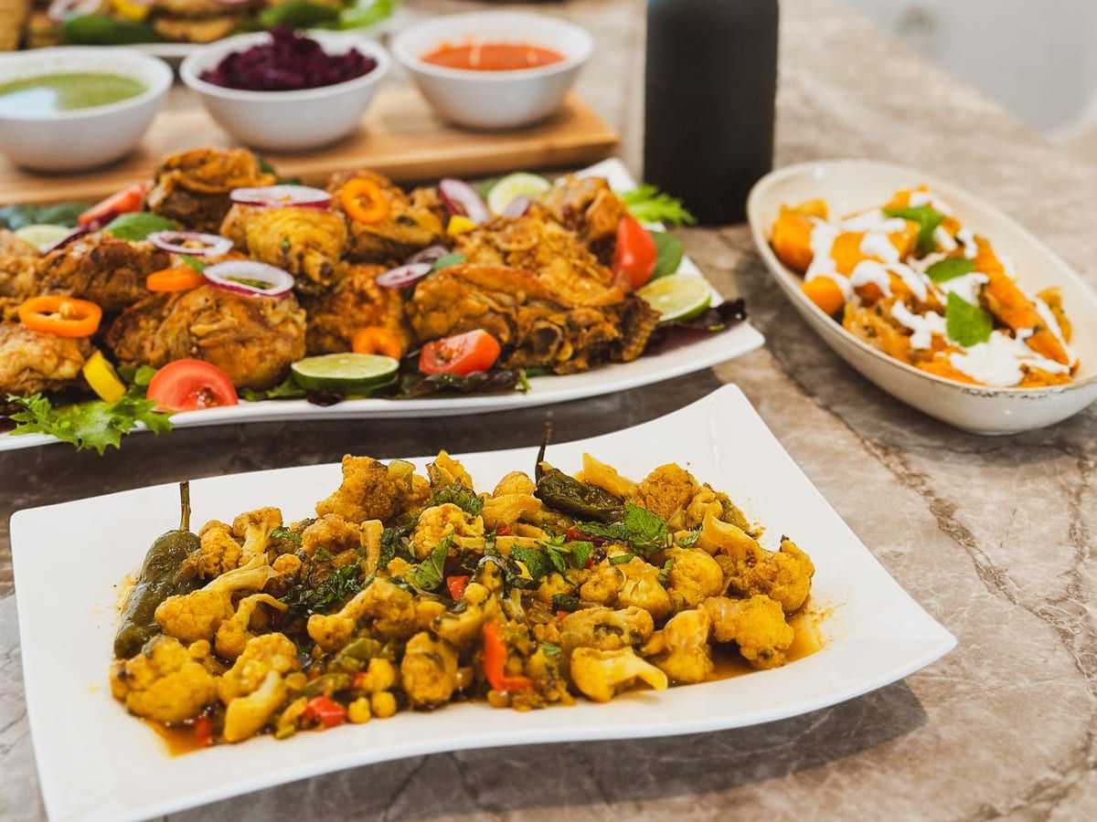 A buffet table with spiced cauliflower, roast chicken, chutneys and salads