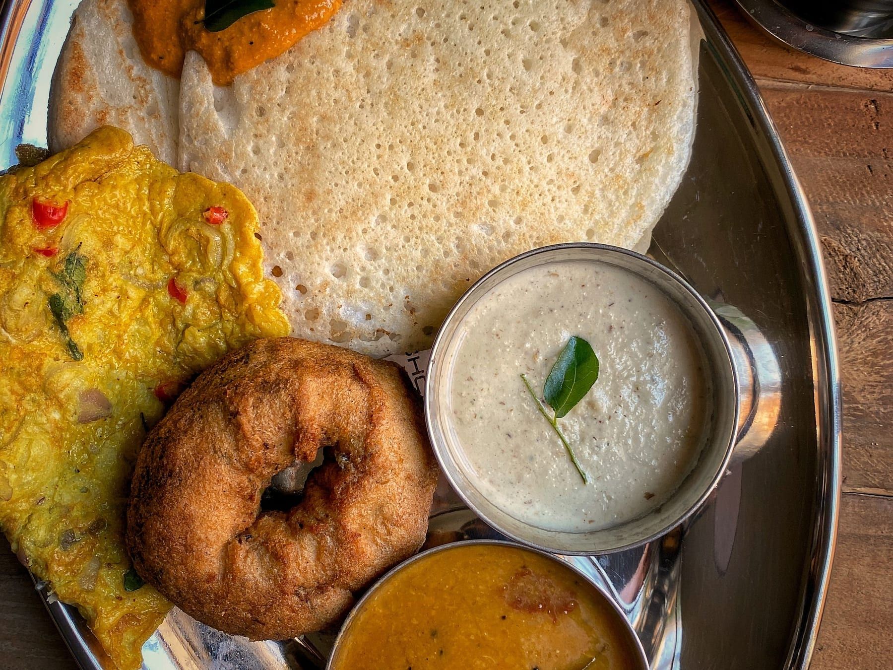 A dosa, a medu vada, coconut chutney and sambar on a steel plate