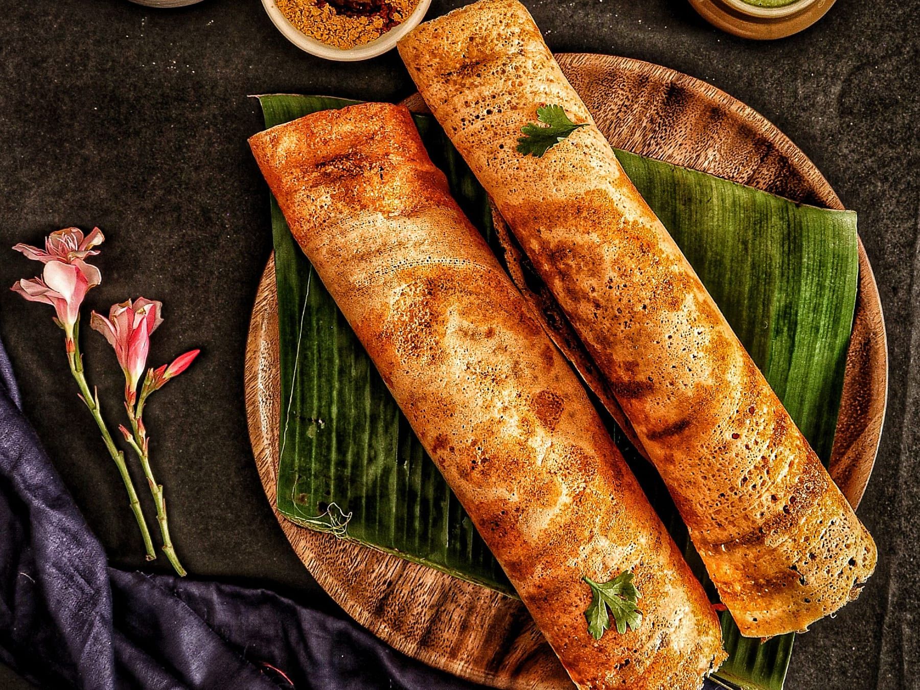 Two dosas on a banana leaf, with chutneys in clay pots